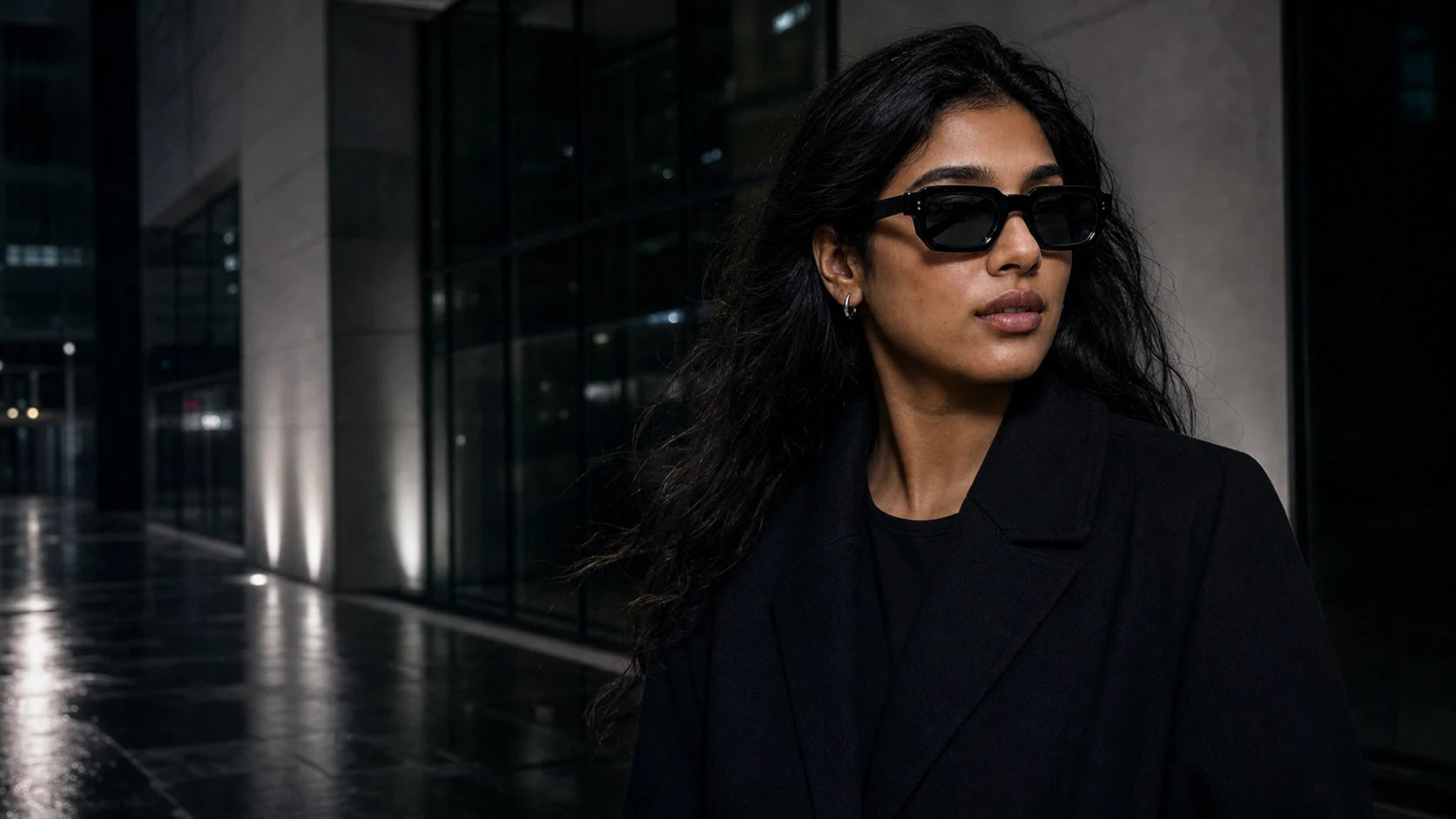 Model wearing black angular NOCT sunglasses in a graphite city at night