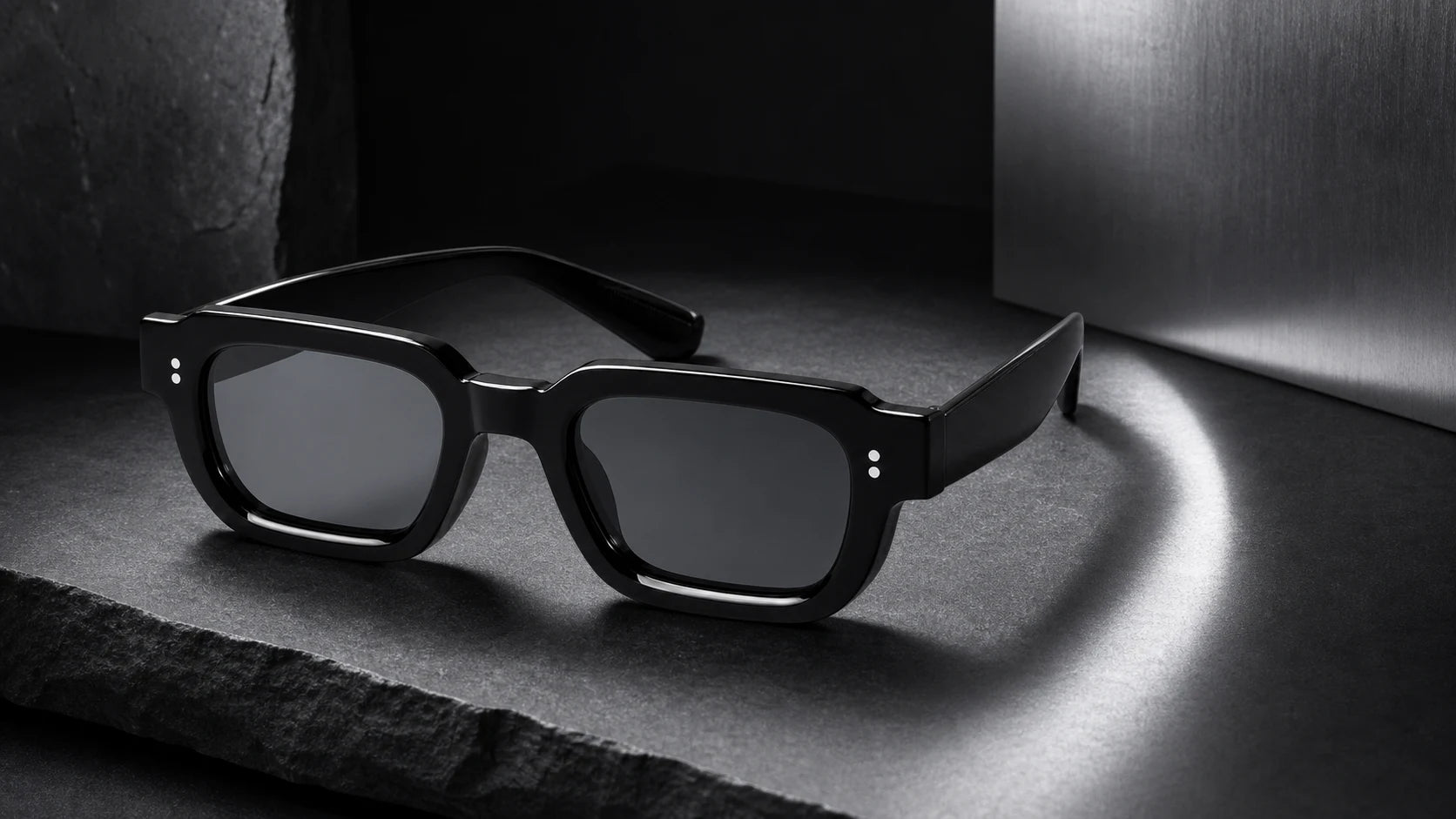 Black angular NOCT sunglasses photographed on graphite stone and cold silver
